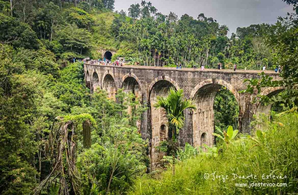 Arcos de pedra, vegetação verdejante e turistas na Ponte dos Nove Arcos, no Ella, Sri Lanka.