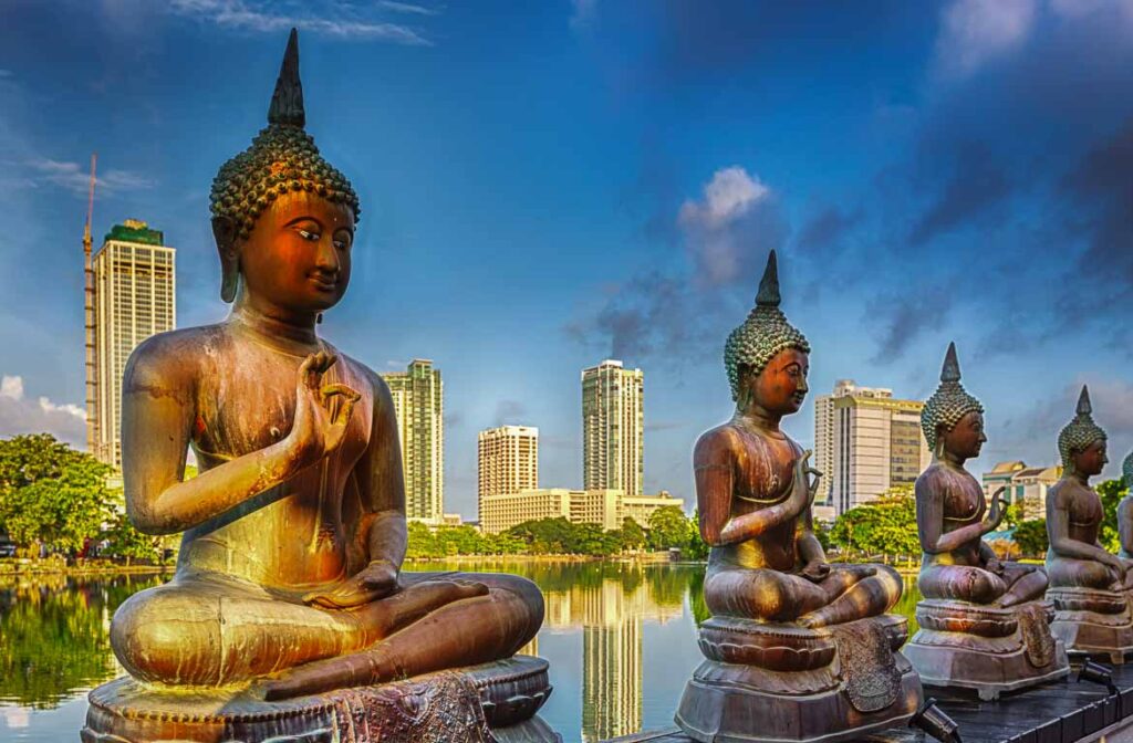 Estátuas imponentes de Buda, em Colombo, Templo Seema Malaka, Sri Lanka, refletem-se numa lagoa serena, num cenário de edifícios modernos.