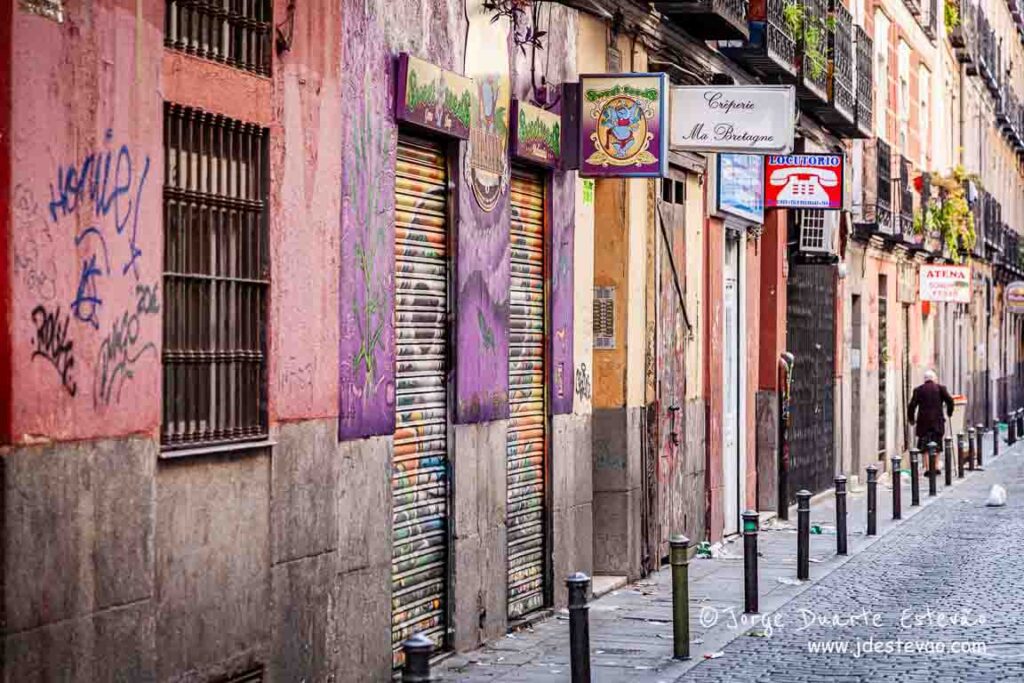 Rua estreita e vibrante no bairro de Malasaña em Madrid, com grafittis, fachadas coloridas e lojas locais que captam a alma alternativa da cidade.