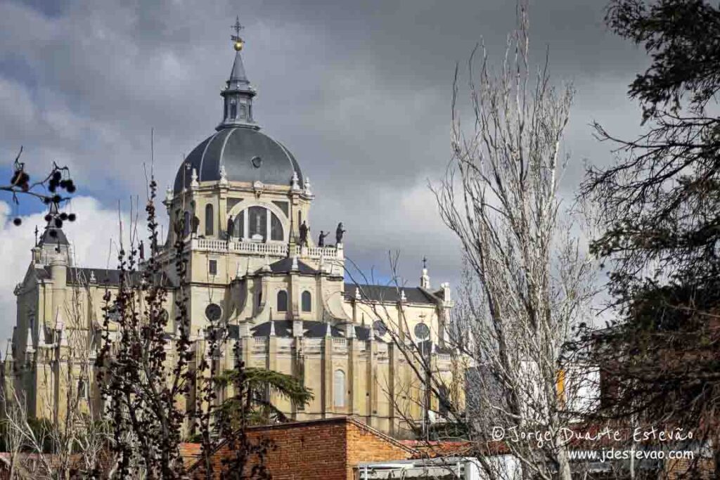 Catedral de Santa Maria a Real de Almudena vista por entre árvores de inverno em Madrid, Espanha. Arquitetura religiosa imponente no centro histórico de Madrid.
