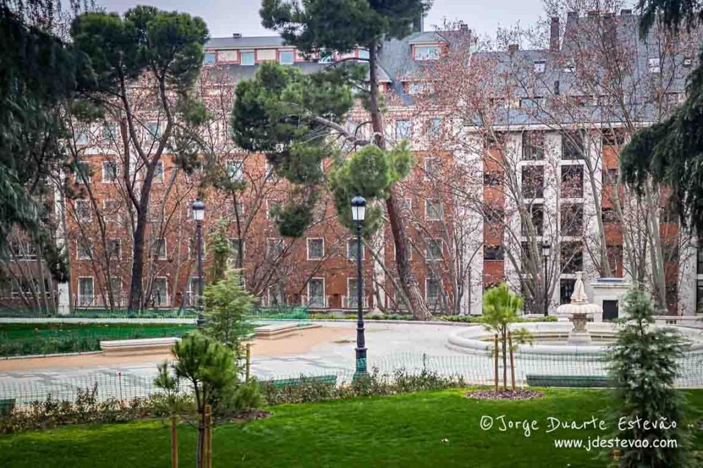 Caminho de terra nos Jardins Sabatini em Madrid, ladeado por sebes de buxo baixas e árvores com folhagem de outono seca e verdes.