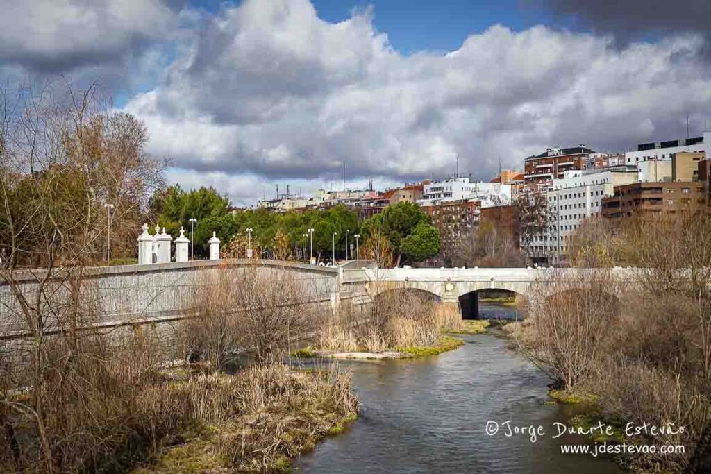 Vista frontal da Ponte do Rei em Madrid, uma ponte de pedra monumental com lanternas clássicas que atravessa o Rio Manzanares. Localizada junto à entrada da Casa de Campo.