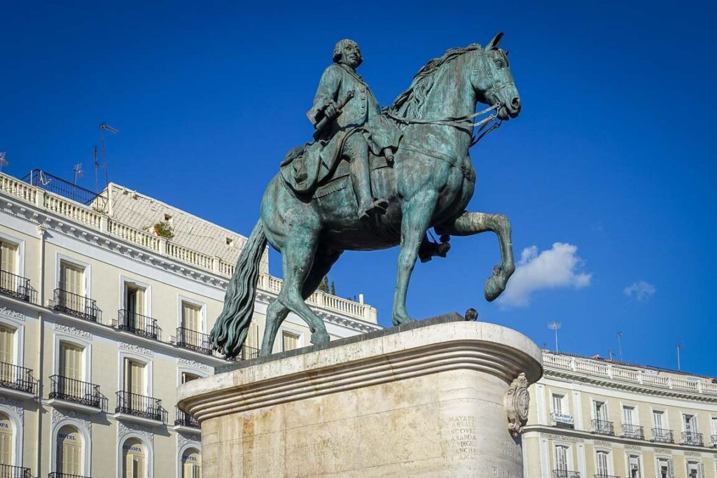 Vista da Puerta del Sol em Madrid, destacando o edifício da Real Casa de Correos e o icónico relógio da torre sob um céu azul. O ponto central para quem decide visitar Madrid.